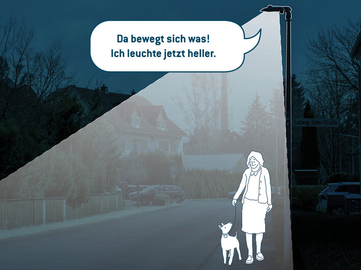 Eine Frau und ihr Hund machen in der Dämmerung einen Spaziergang in einem Wohngebiet. Straße und Bürgersteig sind hell erleuchtet.