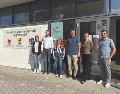 Personen vor Gebäude mit Aufschrift Verwaltungsgemeinschaft Sigmarszell